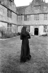 a woman in a black dress standing in front of a large house