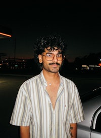 a man in a striped shirt standing in front of a car