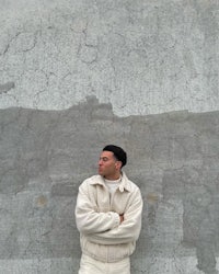 a man in a white jacket leaning against a wall