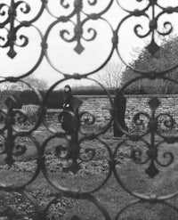 a black and white photo of a woman standing behind a fence