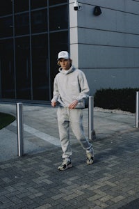 a man in a grey hoodie and sneakers walking down a sidewalk