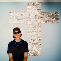 a man in sunglasses standing in front of a wall with a cross on it