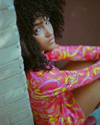 a young woman in a colorful dress leaning against a brick wall