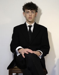 a young man in a suit sitting on a chair