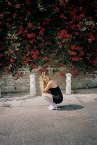 a woman crouching down in front of a flower wall