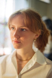 a woman in a white shirt is staring out of a window