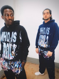 two men standing next to each other wearing hoodies