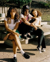 three young people sitting on a bench in a park