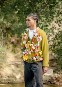 a young man in a green sweater standing next to a river