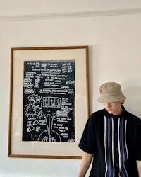 a man in a hat standing next to a framed drawing