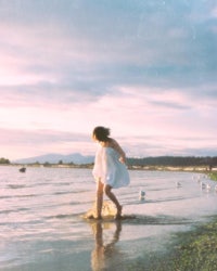 a girl in a white dress walking in the water