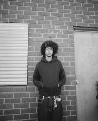 a man in a hoodie standing in front of a brick wall