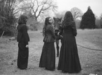 three women in long black dresses standing next to a horse