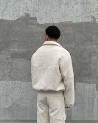 a man is standing in front of a wall wearing a white jacket