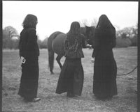 three women standing next to a horse in a field