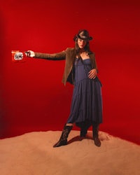 a woman in a blue dress holding a gun in the sand